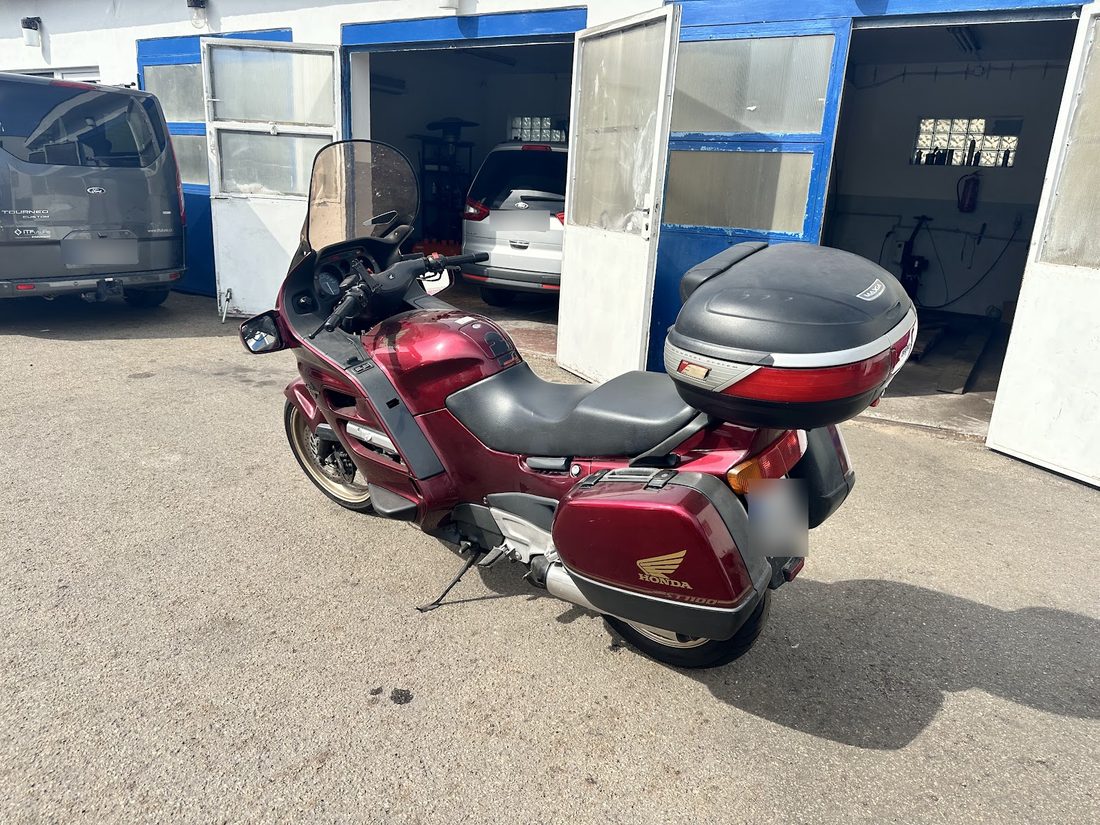 Vínová motorka Honda před otevřenými modrými vraty dílny, vlevo dodávka, v dílně auto